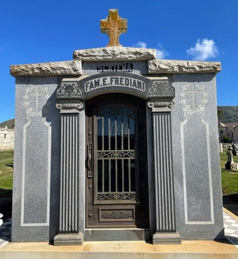 Front view of a small family mausoleum with columns at the entrance and a cross above the door