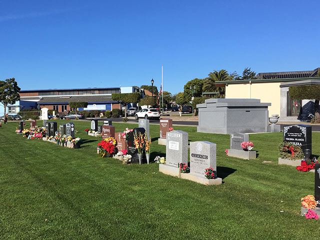 View of cemetery burial grounds where there are many upright grave markers and a small family mausoleum