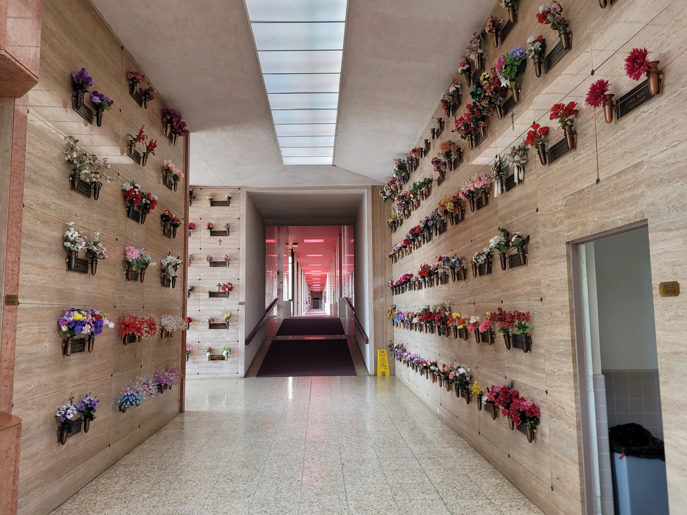 el-camino-mausoleum-interior2 Interior view of a long hallway in the El Camino Mausoleum. Each side of the hall is flanked by brown granite niches with bronze name plates and flower arrangements.