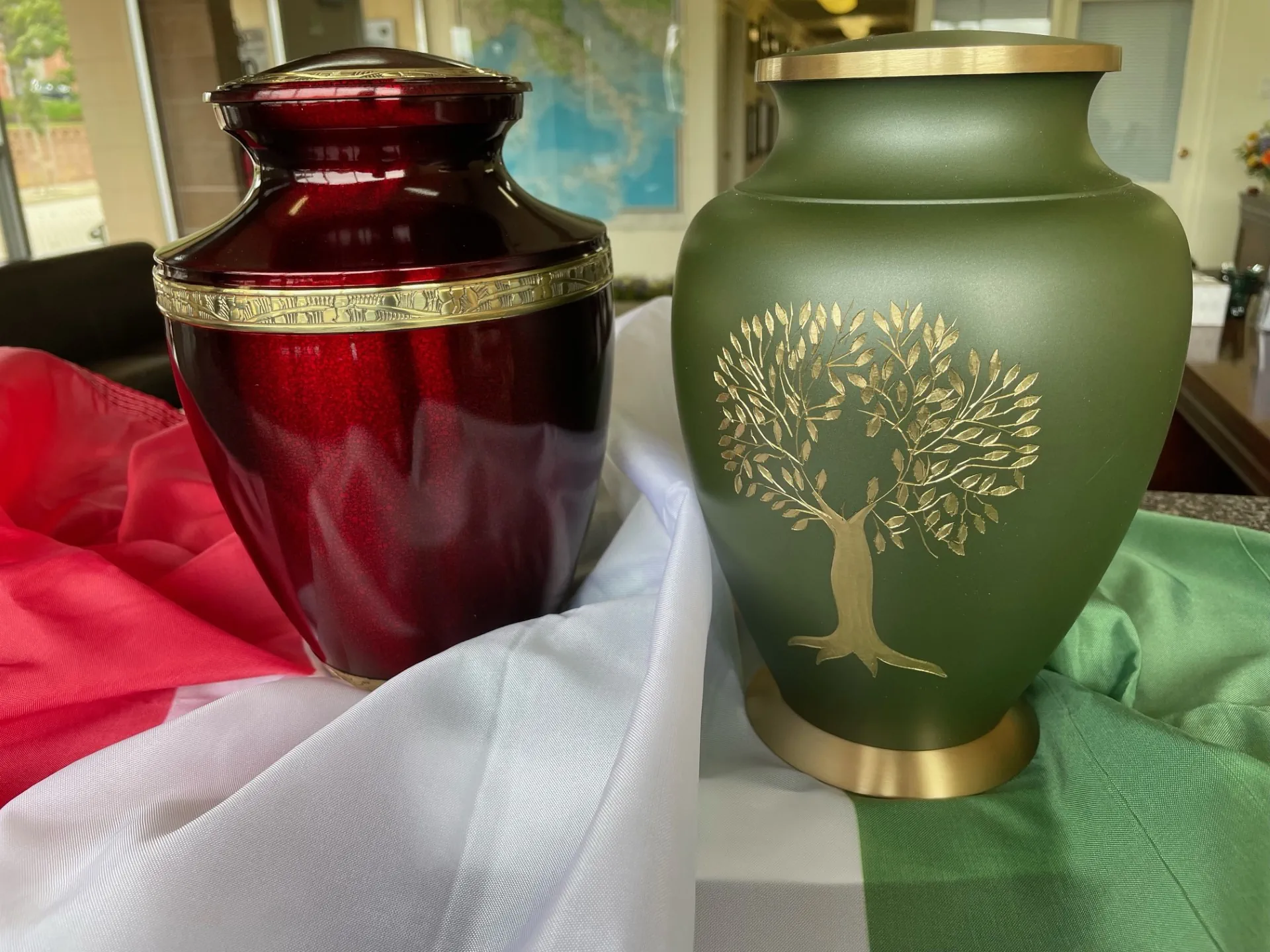 urns Two engraved urns - one is a bold red with gold trim engraved with a vine pattern, the other is green with a gold tree