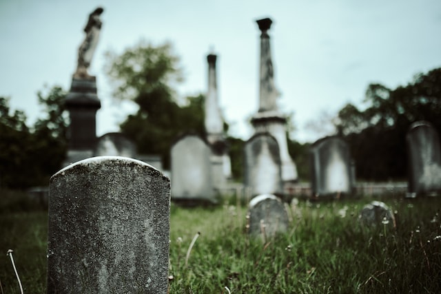Weathered gravestones in an old cemetery with tall monuments and overgrown grass, Daly City, CA.