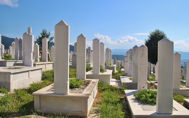 White stone grave markers in a cemetery under a clear blue sky, with distant hills in the background, San Francisco, CA.